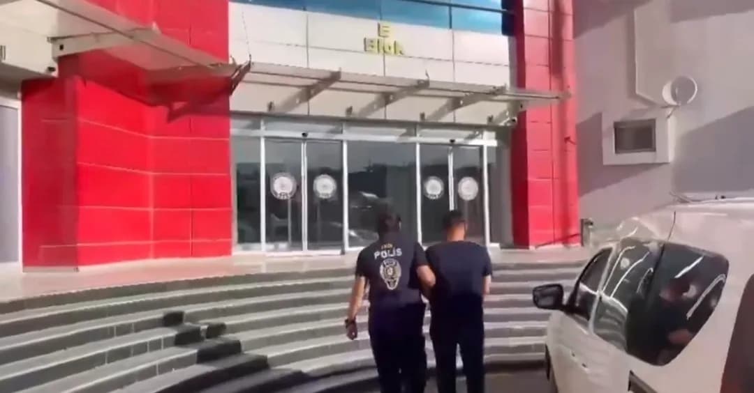 Sırtında POLİS yazılı yeleği bulunan bir polis, gözaltındaki bir kişiyi emniyet binasına götürüyor