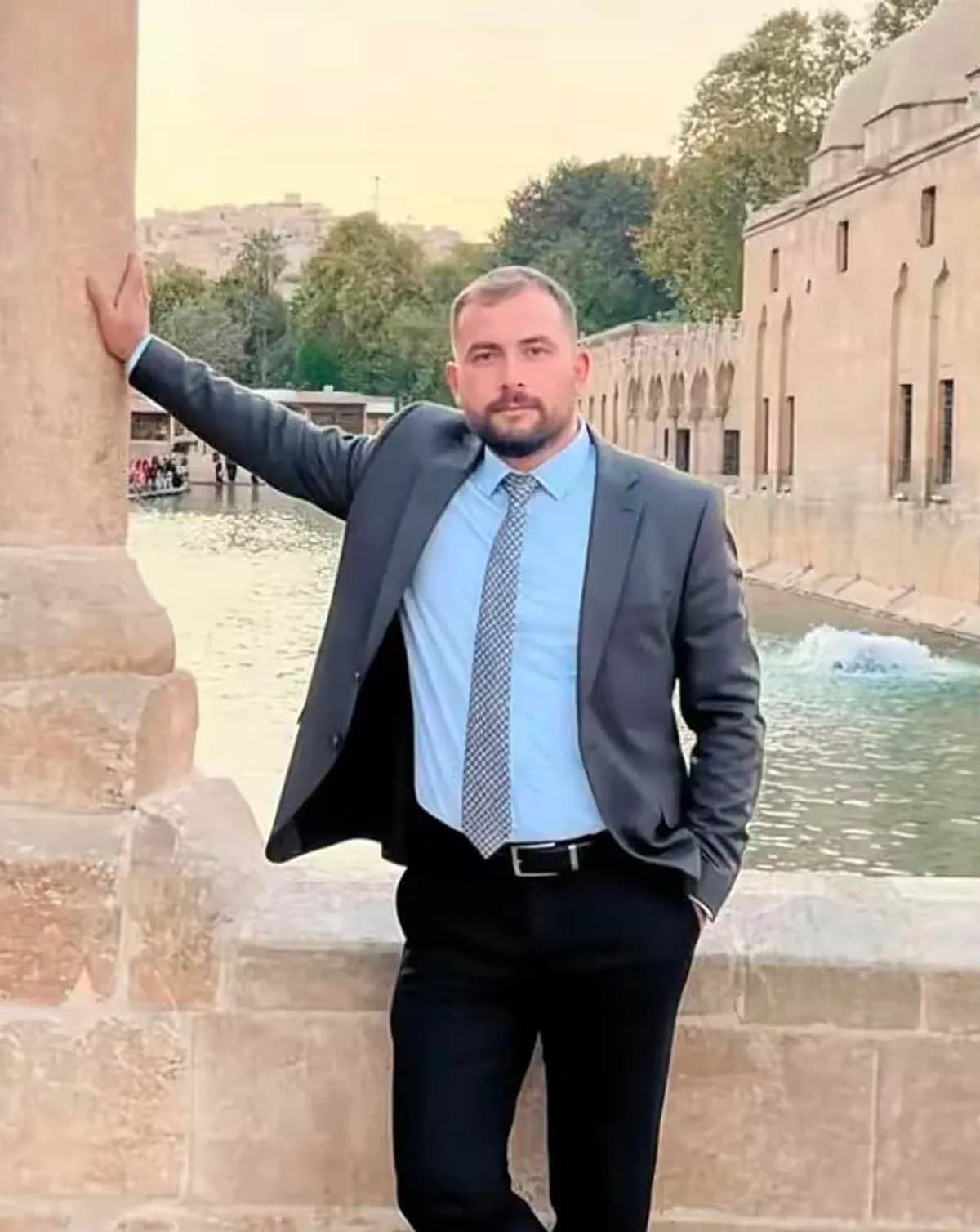Takım elbiseli sakallı bir adam tarihi havuz kenarında poz veriyor