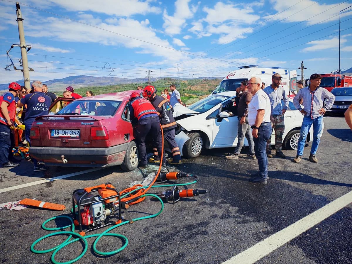Kaza yerinde çarpışan kırmızı ve beyaz otomobiller ile müdahale eden itfaiye ve sağlık ekipleri