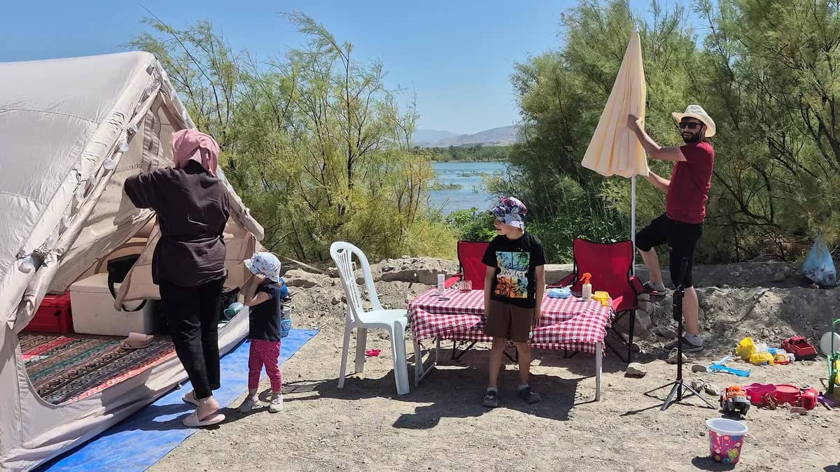 Baraj gölü kıyısında kamp kuran aile, çadır ve şemsiye kurulumu yapıyor